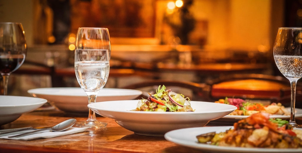 Host a Dinner A nicely-set table with several plates of food and wine glasses with wine and water.